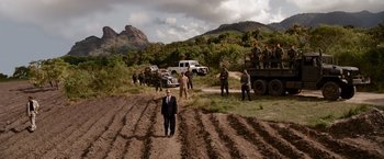 Movie still from “The Expendables” (2010), directed by Sylvester Stallone – A group of men in suits and military vehicles on a dirt road; Extreme Wide shot, High angle
