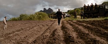 Movie still from “The Expendables” (2010), directed by Sylvester Stallone – A man in a suit walking across a dirt field; Extreme Wide shot, Over the shoulder angle