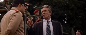 Movie still from “The Expendables” (2010), directed by Sylvester Stallone – A man in a suit and tie pointing at something; Medium shot, Over the shoulder angle
