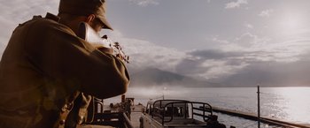 Movie still from “The Expendables” (2010), directed by Sylvester Stallone – A man with a hat on holding a violin in front of a body of water; Medium shot, Low angle