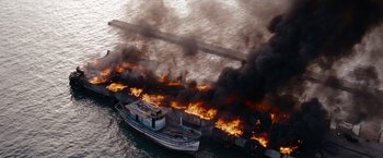 Movie still from “The Expendables” (2010), directed by Sylvester Stallone – An aerial view of a boat on fire in the water; Extreme Wide shot, High angle