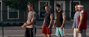 Movie still from “The Expendables” (2010), directed by Sylvester Stallone – A group of young men standing on a tennis court holding rackets; Medium shot, Over the shoulder angle