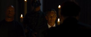 Movie still from “The Expendables” (2010), directed by Sylvester Stallone – A man wearing a suit and tie in the dark; Close Up shot, Over the shoulder angle