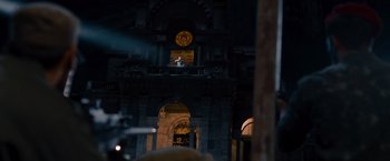 Movie still from “The Expendables” (2010), directed by Sylvester Stallone – A man is standing on a stage in front of a clock; Extreme Wide shot, Low angle