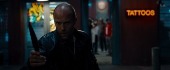 Movie still from “The Expendables” (2010), directed by Sylvester Stallone – A man with a bald head is standing in the dark; Close Up shot, Over the shoulder angle