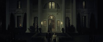 Movie still from “The Fall of the House of Usher” (2023), directed by Mike Flanagan – Two people standing in front of a building at night; Extreme Wide shot, Low angle