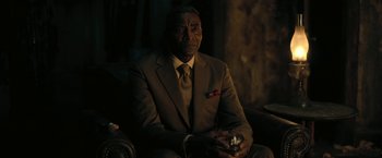 Movie still from “The Fall of the House of Usher” (2023), directed by Mike Flanagan – A man in a suit and tie sitting in a chair holding a glass; Close Up shot, Over the shoulder angle