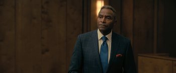 Movie still from “The Fall of the House of Usher” (2023), directed by Mike Flanagan – A man in a suit and tie standing in front of a wooden wall; Close Up shot, Over the shoulder angle