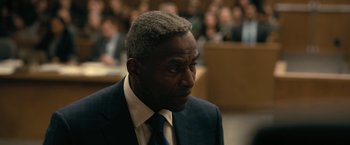 Movie still from “The Fall of the House of Usher” (2023), directed by Mike Flanagan – A man in a suit and tie in front of a group of people; Close Up shot, Over the shoulder angle