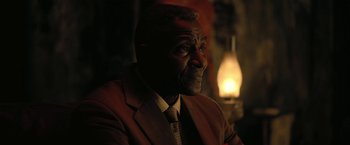 Movie still from “The Fall of the House of Usher” (2023), directed by Mike Flanagan – A man wearing a suit and tie sitting in front of a lamp; Close Up shot, Over the shoulder angle