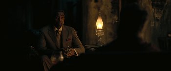 Movie still from “The Fall of the House of Usher” (2023), directed by Mike Flanagan – A man in a suit sitting in front of an oil lamp; Medium shot, Over the shoulder angle