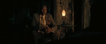 Movie still from “The Fall of the House of Usher” (2023), directed by Mike Flanagan – A man in a suit sitting in front of an oil lamp; Medium shot, Over the shoulder angle