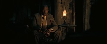 Movie still from “The Fall of the House of Usher” (2023), directed by Mike Flanagan – A man in a suit sitting in front of an oil lamp; Medium shot, Over the shoulder angle