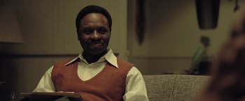 Movie still from “The Fall of the House of Usher” (2023), directed by Mike Flanagan – A man sitting on a couch in a room; Close Up shot, Over the shoulder angle