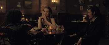 Movie still from “The Fall of the House of Usher” (2023), directed by Mike Flanagan – A woman sitting at a table with a glass of wine; Medium shot, Over the shoulder angle