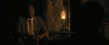 Movie still from “The Fall of the House of Usher” (2023), directed by Mike Flanagan – A man sitting in front of an oil lamp in a dark room; Medium shot, Over the shoulder angle