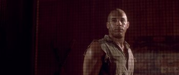Movie still from “The Fast and the Furious” (2001), directed by Rob Cohen – A bald man in a brown shirt is behind a fence; Close Up shot, Low angle