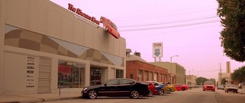 Movie still from “The Fast and the Furious” (2001), directed by Rob Cohen – Cars parked on the side of the street in front of a building; Extreme Wide shot, Low angle