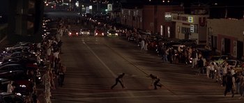 Movie still from “The Fast and the Furious” (2001), directed by Rob Cohen – Two skateboarders cross a street at night with cars parked on the side of the road; Extreme Wide shot, High angle