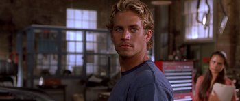 Movie still from “The Fast and the Furious” (2001), directed by Rob Cohen – A man with blonde hair is standing in a room; Close Up shot, Over the shoulder angle