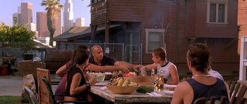Movie still from “The Fast and the Furious” (2001), directed by Rob Cohen – A group of people sitting at a table with a bowl of food; Wide shot, Over the shoulder angle
