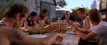 Movie still from “The Fast and the Furious” (2001), directed by Rob Cohen – A group of people sitting at a table drinking beer; Medium shot, Low angle