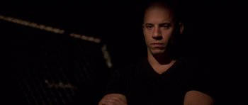 Movie still from “The Fast and the Furious” (2001), directed by Rob Cohen – A man in a black shirt is looking at the camera; Close Up shot, Over the shoulder angle