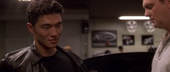 Movie still from “The Fast and the Furious” (2001), directed by Rob Cohen – A man in a black t - shirt is looking at the camera; Close Up shot, Over the shoulder angle