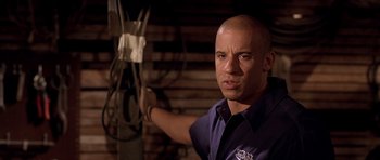 Movie still from “The Fast and the Furious” (2001), directed by Rob Cohen – A bald man in a blue shirt is posing for a picture; Close Up shot, Low angle