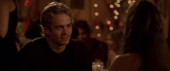 Movie still from “The Fast and the Furious” (2001), directed by Rob Cohen – A man sitting at a table with a drink in front of him; Close Up shot, Over the shoulder angle
