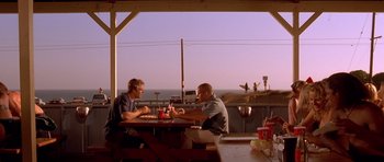 Movie still from “The Fast and the Furious” (2001), directed by Rob Cohen – Two men are sitting at a table outside; Wide shot, Low angle
