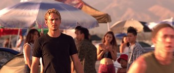 Movie still from “The Fast and the Furious” (2001), directed by Rob Cohen – A group of people standing on top of a sandy beach; Medium shot, Over the shoulder angle
