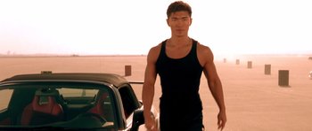 Movie still from “The Fast and the Furious” (2001), directed by Rob Cohen – A man in a black tank top standing next to a car; Medium shot, Low angle