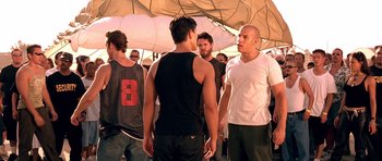 Movie still from “The Fast and the Furious” (2001), directed by Rob Cohen – A group of men standing under an umbrella; Medium shot, Over the shoulder angle