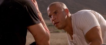Movie still from “The Fast and the Furious” (2001), directed by Rob Cohen – A bald man is looking at a man with blood all over his arm; Close Up shot, Over the shoulder angle