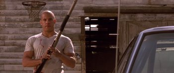 Movie still from “The Fast and the Furious” (2001), directed by Rob Cohen – A man holding a baseball bat while standing in front of a building; Medium shot, Low angle