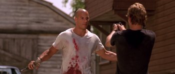 Movie still from “The Fast and the Furious” (2001), directed by Rob Cohen – A bald man with blood all over his shirt; Medium shot, Over the shoulder angle