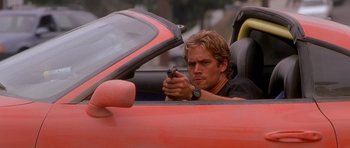Movie still from “The Fast and the Furious” (2001), directed by Rob Cohen – A man holding a gun while sitting in a red car; Close Up shot, Over the shoulder angle