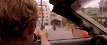 Movie still from “The Fast and the Furious” (2001), directed by Rob Cohen – A man holding a gun while riding a motorcycle down a street; Close Up shot, Over the shoulder angle