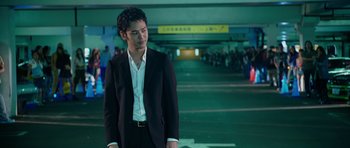 Movie still from “The Fast and the Furious: Tokyo Drift” (2006), directed by Justin Lin – A man in a black suit standing in a parking lot; Medium shot, Low angle
