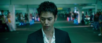 Movie still from “The Fast and the Furious: Tokyo Drift” (2006), directed by Justin Lin – A man in a black suit standing in a parking lot; Close Up shot, Low angle