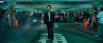 Movie still from “The Fast and the Furious: Tokyo Drift” (2006), directed by Justin Lin – A man in a black suit is standing in a parking lot; Wide shot, Low angle