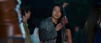 Movie still from “The Fast and the Furious: Tokyo Drift” (2006), directed by Justin Lin – A man in a black jacket is standing in front of a group of people; Medium shot, Over the shoulder angle