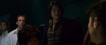 Movie still from “The Fast and the Furious: Tokyo Drift” (2006), directed by Justin Lin – A man with long black hair standing next to another man; Medium shot, Over the shoulder angle