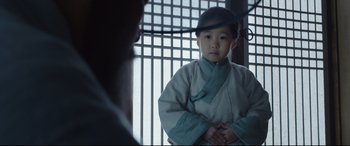Movie still from “The Fortress” (2017), directed by Hwang Dong-hyuk – A young asian boy in traditional garb in front of an iron gate; Medium shot, Over the shoulder angle