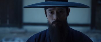 Movie still from “The Fortress” (2017), directed by Hwang Dong-hyuk – A man with a long beard wearing a black hat; Close Up shot, Low angle