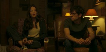 Movie still from “The Girl in the Mirror” (2022), created by Sergio G. Sánchez – A man and a woman sitting on a couch; Medium shot, Over the shoulder angle