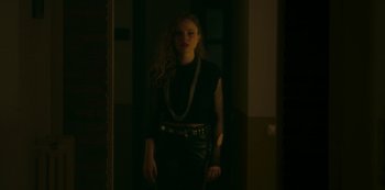 Movie still from “The Girl in the Mirror” (2022), created by Sergio G. Sánchez – A woman standing in a dark room wearing a necklace; Medium shot, Over the shoulder angle