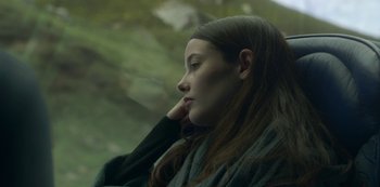 Movie still from “The Girl in the Mirror” (2022), created by Sergio G. Sánchez – A woman sitting in front of a tree looking off into the distance; Close Up shot, Over the shoulder angle