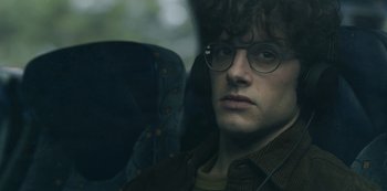 Movie still from “The Girl in the Mirror” (2022), created by Sergio G. Sánchez – A young man wearing glasses sitting in a car seat; Close Up shot, Over the shoulder angle
